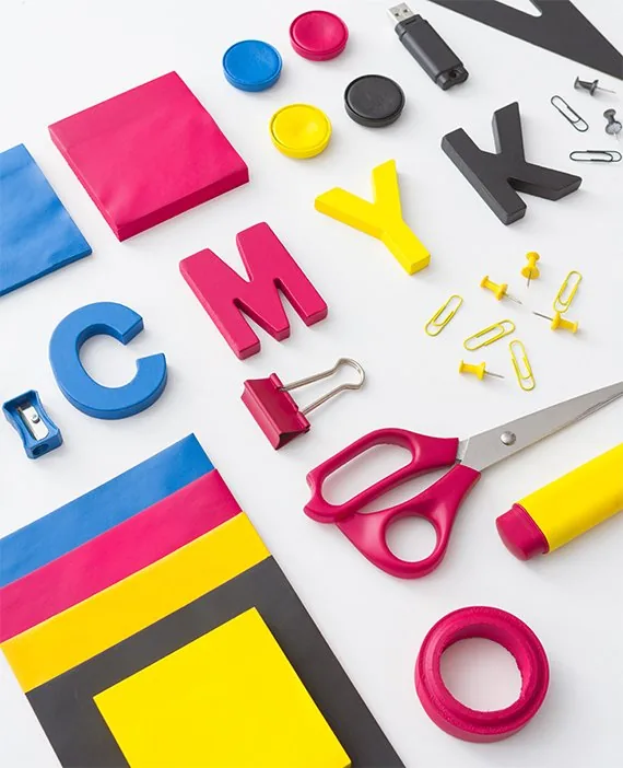 Letras CMYK de colores, clips y tijera sobre una mesa
